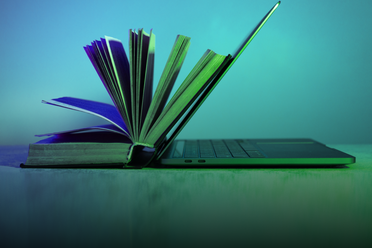 Aufgeschlagenes Buch, das Rücken an Rücken mit einem geöffneten Laptop steht – Symbol für die Verbindung von analogem und digitalem Lernen