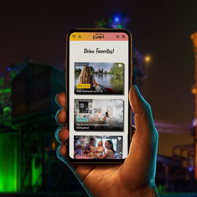 Hand hält ein Smartphone vor Nachtkulisse im Ruhrgebiet. Der Screen zeigt die Anwendung Reisekumpel