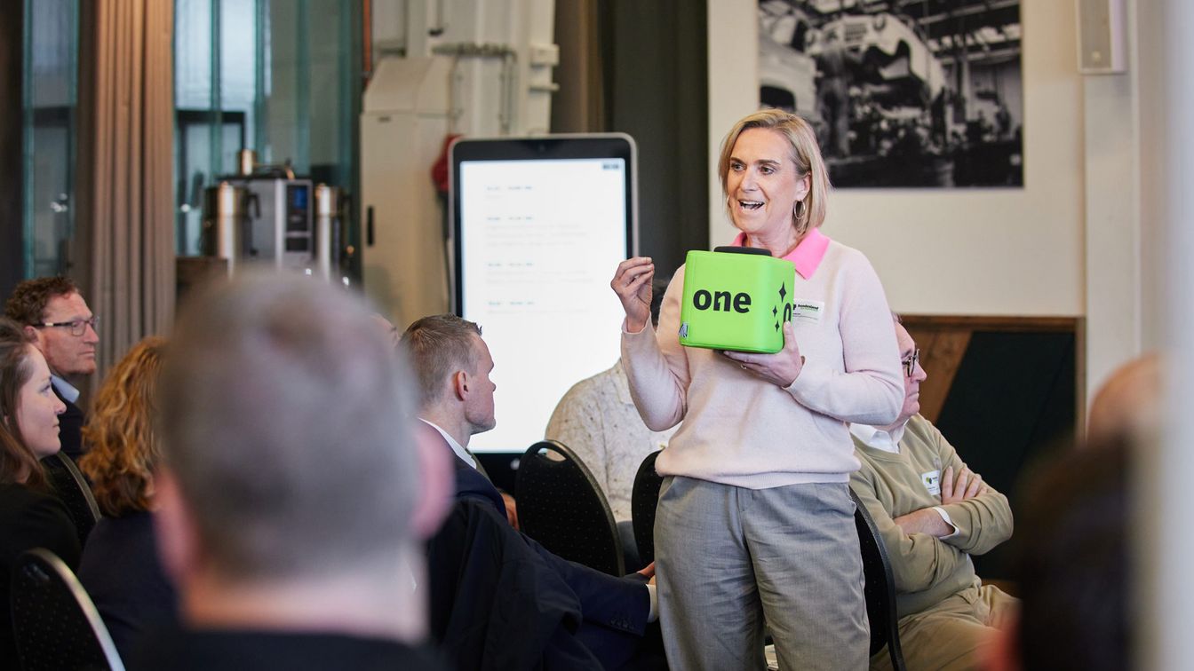 Freie Wortmeldung beim Bundesland KI‑Summit vor Publikum mit einem grünen Mikrofonwürfel mit one‑Branding